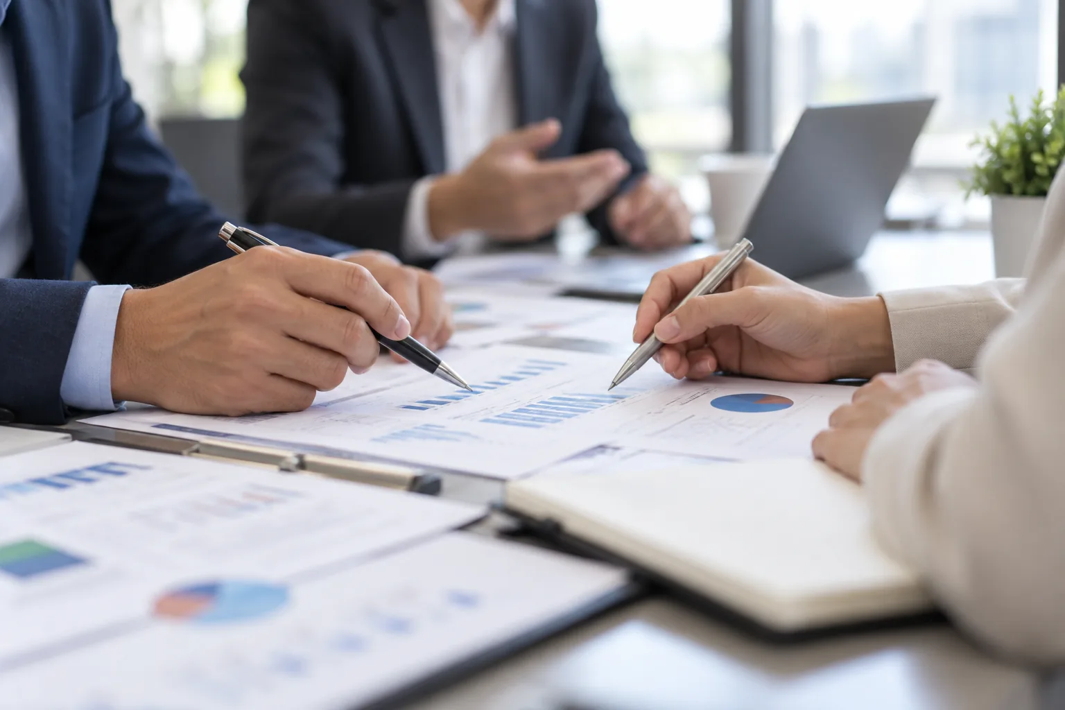 Mains sur des documents et graphiques lors d'une réunion, personnes floues en arrière-plan